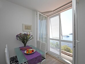 Un balcón con una mesa dispuesta con fruta y flores, vista al mar y un barco en la distancia.