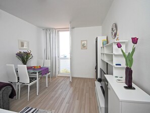 Una sala de estar moderna y bien iluminada con comedor, un sofá blanco, una mesa de centro y un mueble para televisión con televisor de pantalla plana.