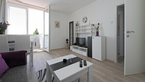 A modern, well-lit living room with a sofa, a coffee table, a TV, and a bookshelf. - Apartment Lavandula - Two-Bedroom Apartment with Sea View (Dubrovnik)
