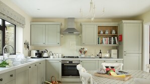 A kitchen with light-colored cabinets, a stove, oven, and a dining area with a table set for two. - Fairfields, Moreton-in-Marsh, sleeps 6 guests  in 3 bedrooms (Moreton-in-Marsh)