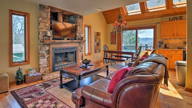 A cozy living room with a stone fireplace, leather sofa, and a dining area with a view. - Beautiful Cabin - Hot Tub & Mtn views - 2 min to Banner Elk & 10 min to ski! (Banner Elk)