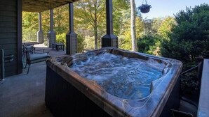 A hot tub in a covered outdoor area with a patio, seating, and a hanging planter. - Beautiful Cabin - Hot Tub & Mtn views - 2 min to Banner Elk & 10 min to ski! (Banner Elk)