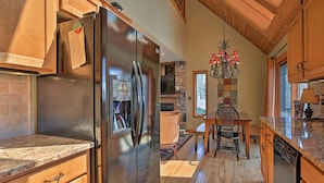 A kitchen with wooden cabinets, a stainless steel refrigerator, a chandelier, and a stone fireplace. - Beautiful Cabin - Hot Tub & Mtn views - 2 min to Banner Elk & 10 min to ski! (Banner Elk)