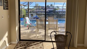 A room with a sliding glass door leading to a pool area, a chair, and a small table. - Gorgeous SW Cape Home on canal w/ pool - Southern Exposure  (Cape Coral)