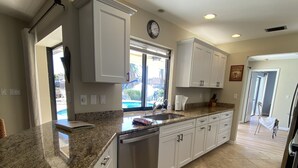 A kitchen with granite countertops, white cabinets, a dishwasher, and a large window. - Gorgeous SW Cape Home on canal w/ pool - Southern Exposure  (Cape Coral)