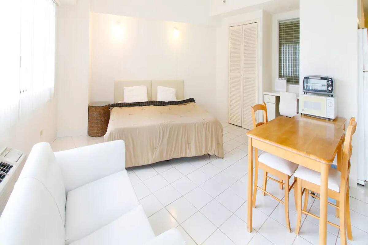 A compact room with a bed, a small dining table with chairs, a kitchenette with a toaster, and a white sofa.