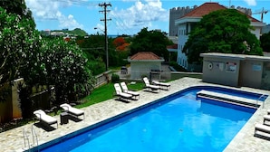 A rectangular swimming pool with a stone tile border, surrounded by lounge chairs and a small garden area. - Pia Resort Hotel Corner Studio Room 1 (Tamuning)