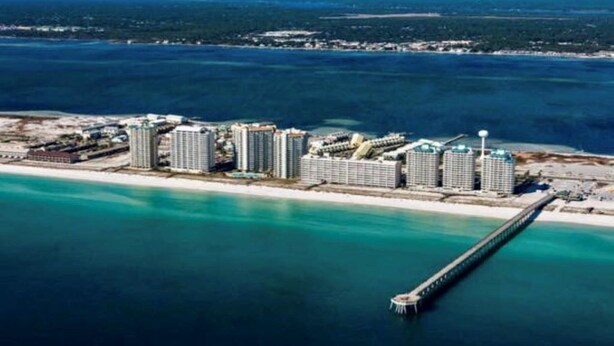 Ein Hotel an der Küste mit mehreren Hochhäusern, einer Pier, die sich ins Wasser erstreckt, und einem Strand.