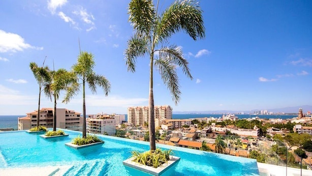A swimming pool with palm trees, a clear sky, and a distant cityscape. - Zenith 601, 2 Balconies, Spectacular Views, in Zona Romantica, Rooftop Pool/Spa (Puerto Vallarta)