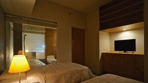 A hotel room with two beds, a TV on a wooden cabinet, a bathroom with a bathtub, and a lamp on a bedside table.