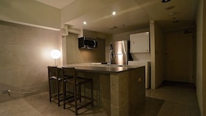 A modern kitchen with a central island, bar stools, stainless steel appliances, and recessed ceiling lighting.