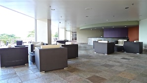 A spacious lobby with high ceilings, large windows, and modern wicker furniture.