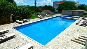 Piscina rectangular con borde de baldosas de piedra, rodeada de sillas de descanso y una pequeña escalera que lleva a una zona cubierta.