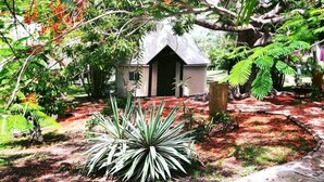 A small house with a sloped roof, surrounded by lush greenery and various plants. - Naina Park Resort (La Foa)