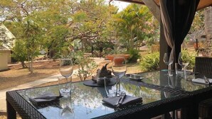 An outdoor dining area with a glass table, chairs, and wine glasses. - Naina Park Resort (La Foa)