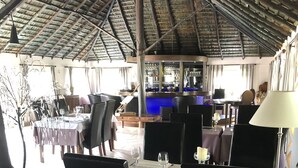 A restaurant with tables set for dining, a bar area, and a thatched roof structure. - Naina Park Resort (La Foa)