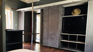 A modern room with a large flat-screen TV mounted on a wall, wooden flooring, and a large bed. - Naina Park Resort (La Foa)
