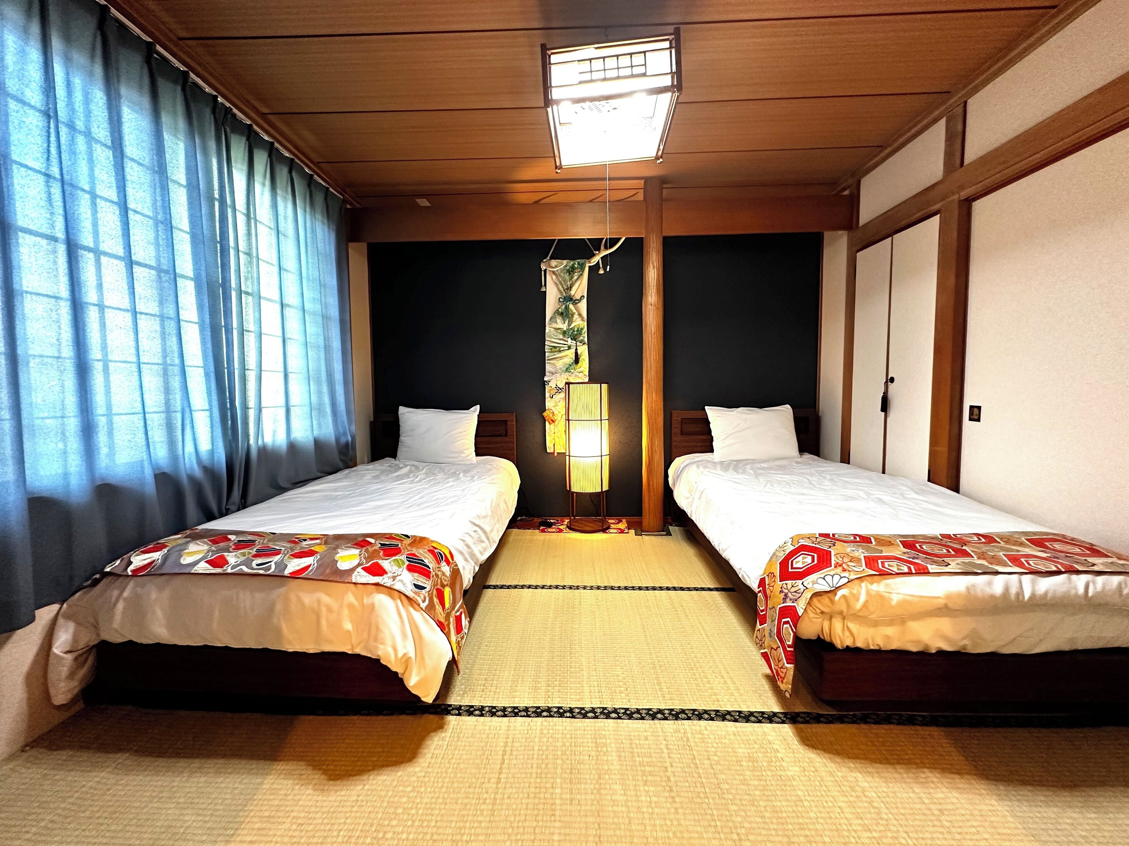 Habitación de hotel con dos camas, suelo de estera de tatami, ventilador de techo y luz nocturna.