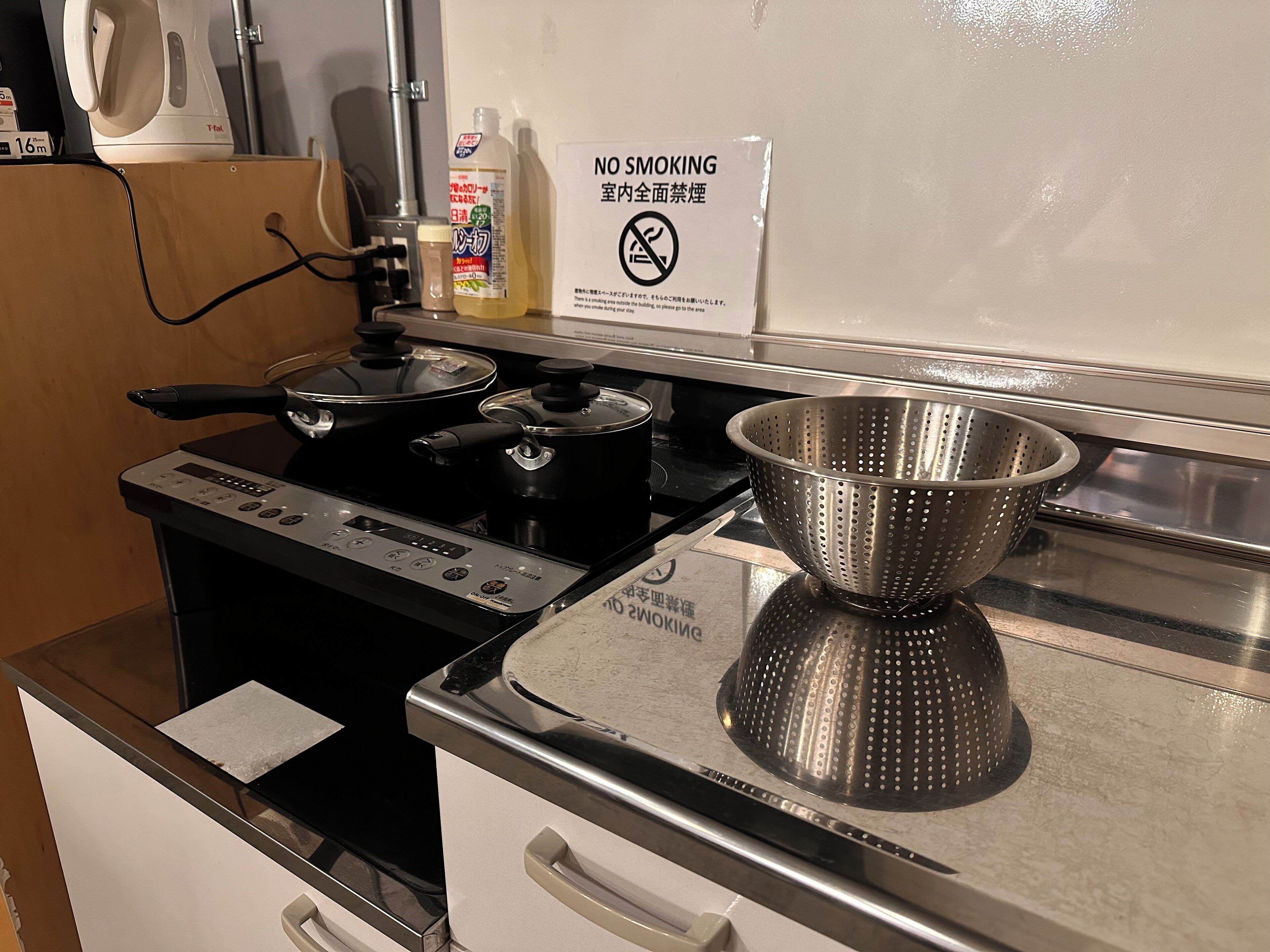 Une cuisine équipée d’une cuisinière, de casseroles, d’une passoire et d’un panneau indiquant « Il est interdit de fumer ».