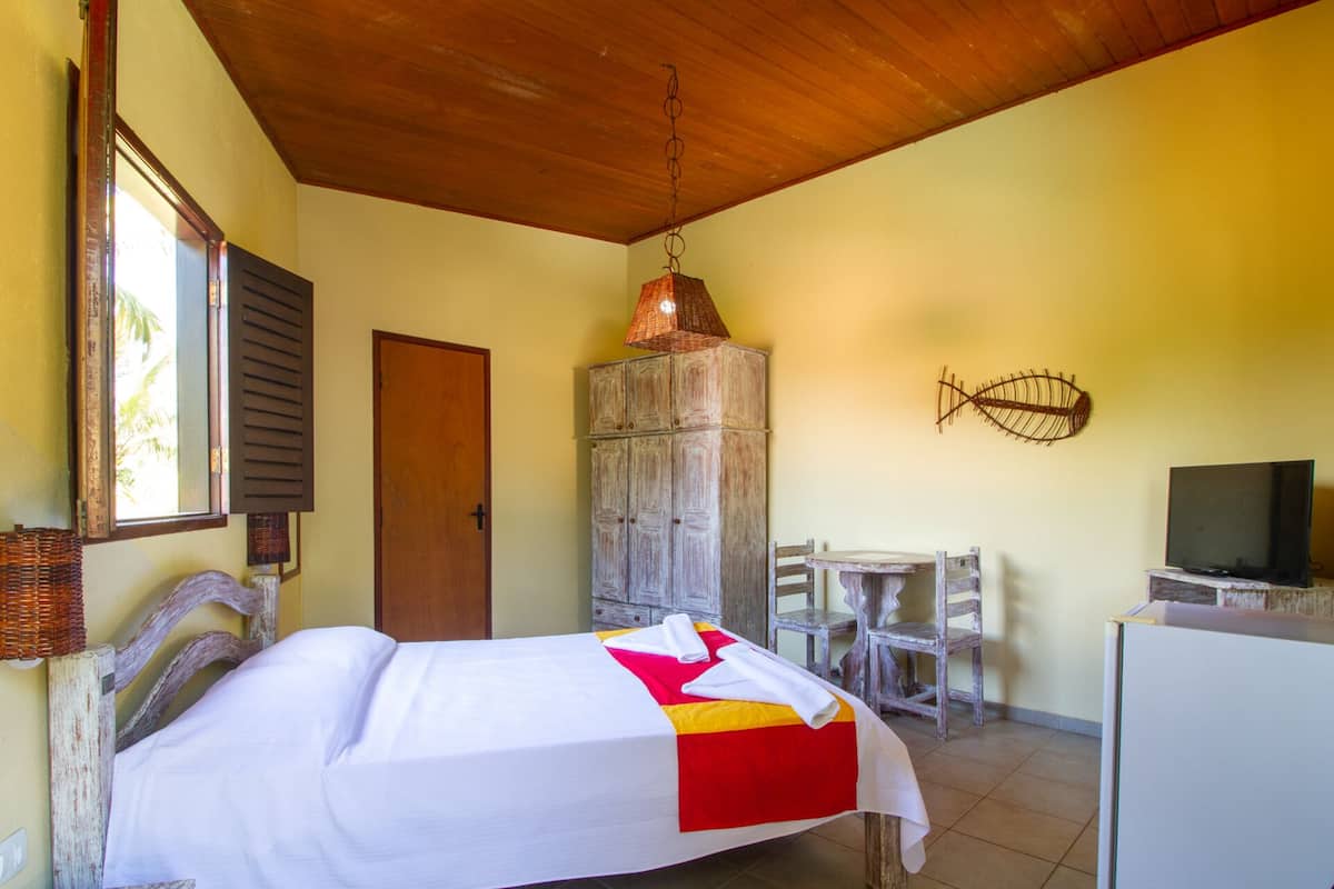 Un dormitorio con cama, un armario de madera, un escritorio con silla, televisor y lámpara colgante.