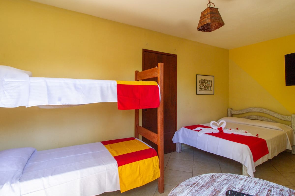 Una habitación con literas, una silla de madera, una mesa y una lámpara colgante.