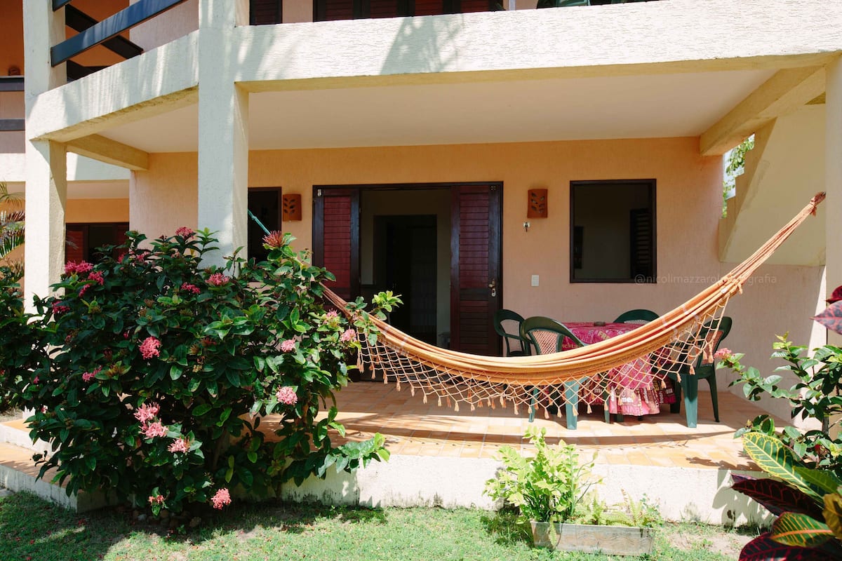 Un espacio al aire libre techado con una hamaca, una mesa con mantel y una silla.