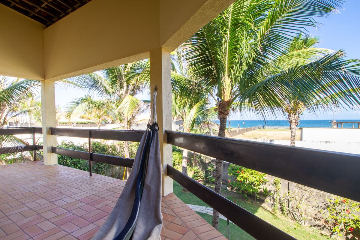 Un balcón con una hamaca, palmeras y vista a la playa y al océano.