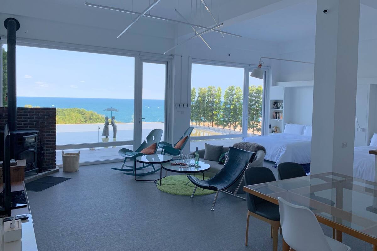 Une chambre d’hôtel moderne dotée d’un grand balcon, d’une cheminée et offrant une vue sur la mer.