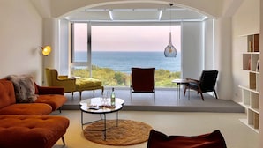 A modern living room with a large window overlooking the sea, featuring a sofa, chairs, a round table, and a hanging light fixture. - Twilight BnB (New Taipei City)