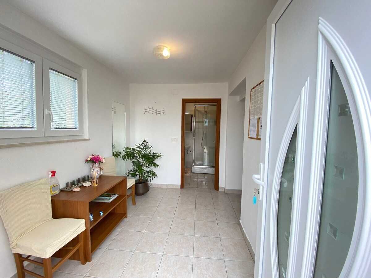A hallway with a sofa, a table with a vase and a plant, and a door leading to a shower area.