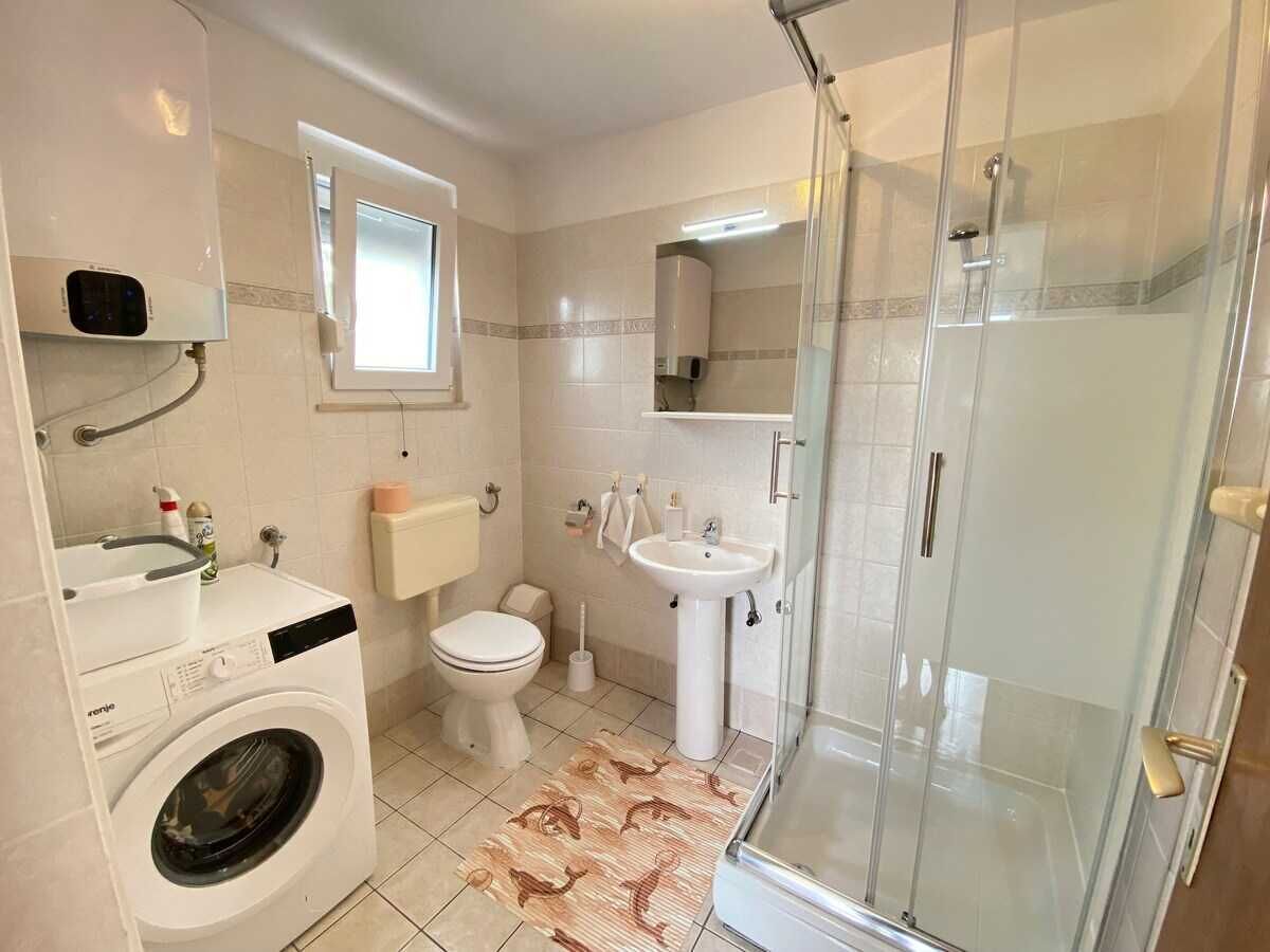 A bathroom with a washing machine, toilet, sink, and glass shower enclosure.