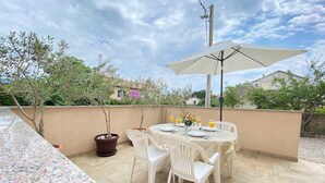 An outdoor patio with a round table, white chairs, and a large umbrella. - Apartment Maticic dole (Silo - island Krk)