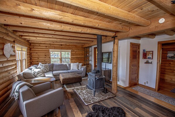 A log cabin interior with a wooden ceiling, a fireplace, a sofa, and a television. - Little Bear Cabin by Hauserman Rentals (Tahoe Vista)
