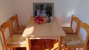 A dining table with two chairs, a framed picture, a bowl of fruit, and two wine glasses.