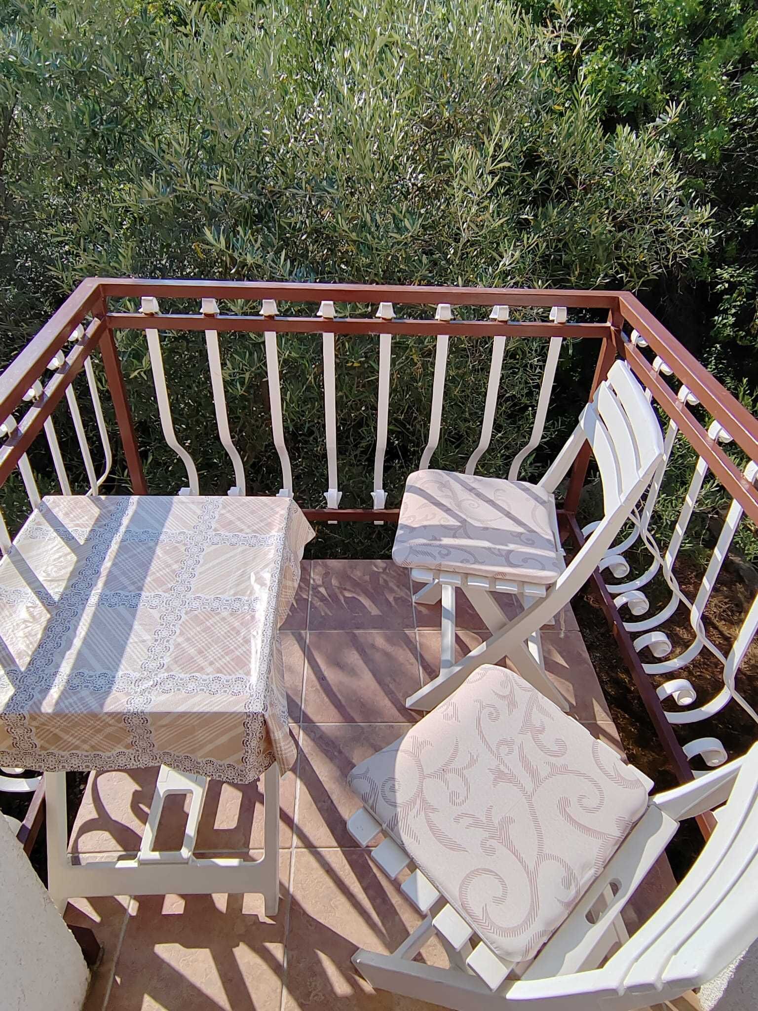 Een balkon met een tafel en twee stoelen, omgeven door een metalen hekwerk.