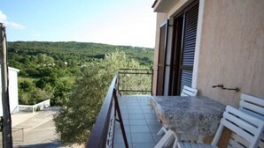 A balcony with a table and chairs, overlooking a green landscape.
