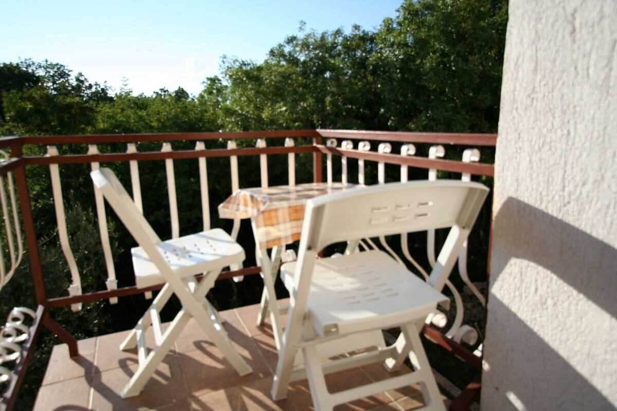Ein Balkon mit weißen Stühlen und einem kleinen Tisch, umgeben von einem Metallgeländer.