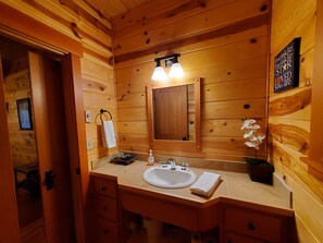 A wooden cabin bathroom with a sink, mirror, towel, and a sign on the wall.