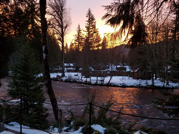 A river with snow-covered banks and trees in the foreground.