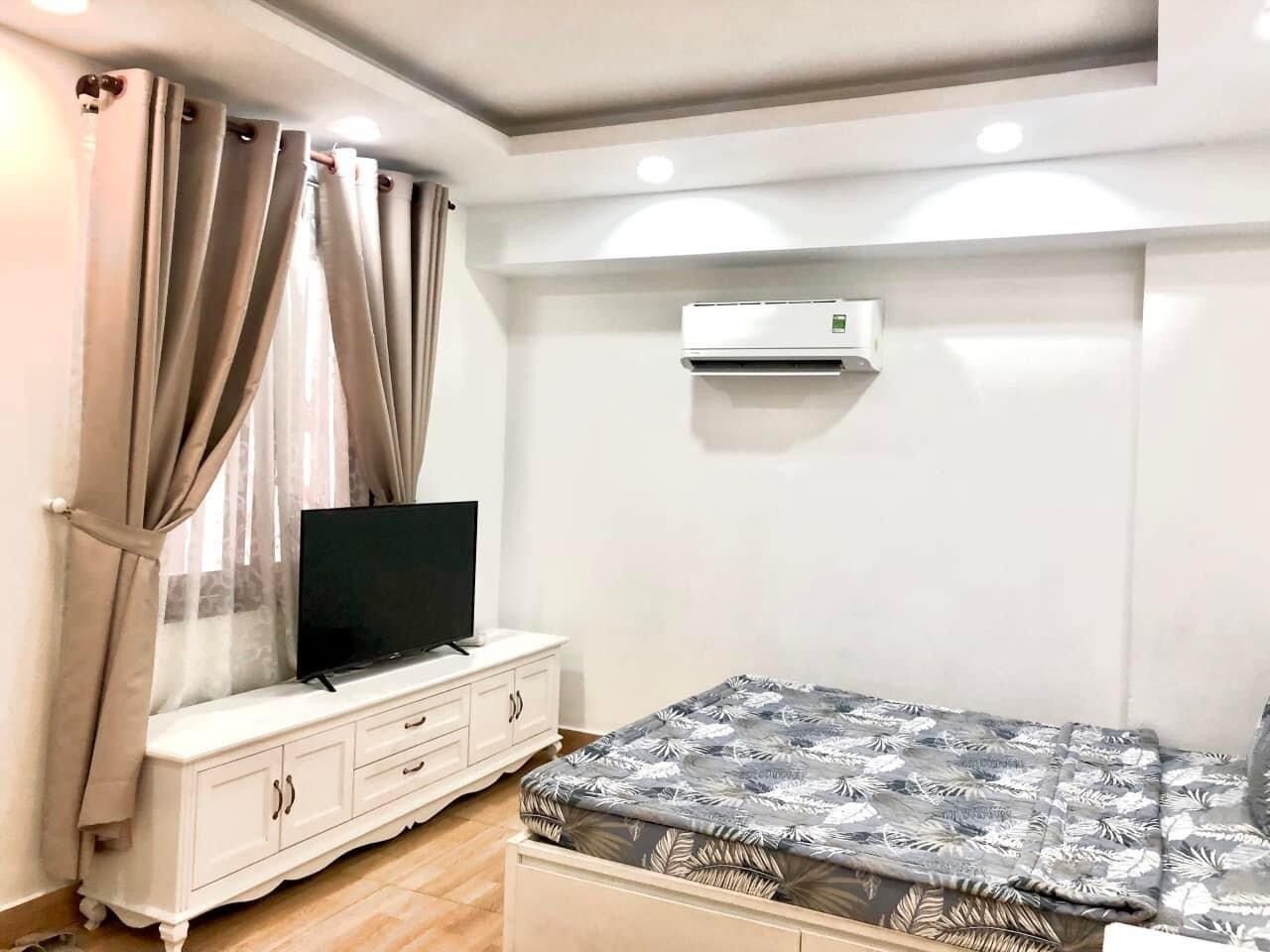 Un dormitorio con una cama, un televisor sobre un tocador blanco y un equipo de aire acondicionado en la pared.