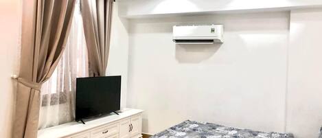 Un dormitorio con una cama, un televisor sobre un tocador blanco y un equipo de aire acondicionado en la pared.