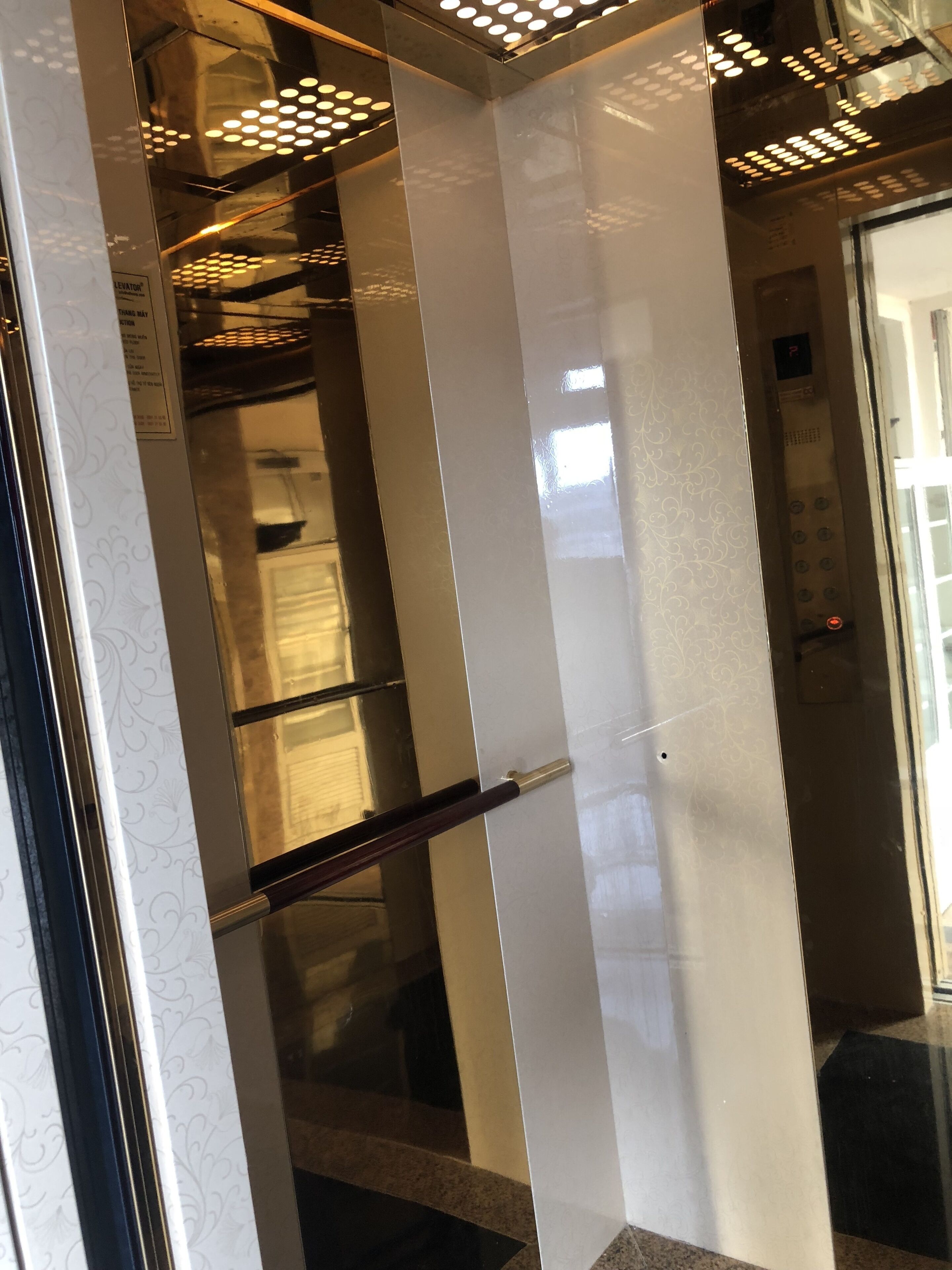 An elevator interior with a glass door, a handrail, and a ceiling with circular lights.