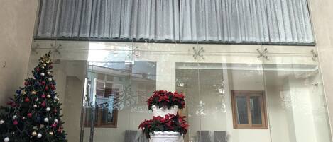 A hotel lobby with a Christmas tree, potted plants, and a large window with curtains.