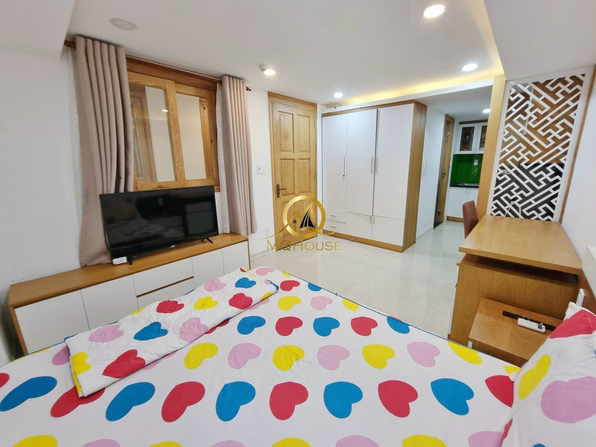 Camera da letto moderna con TV, armadio e letto con copriletto a pois colorati.