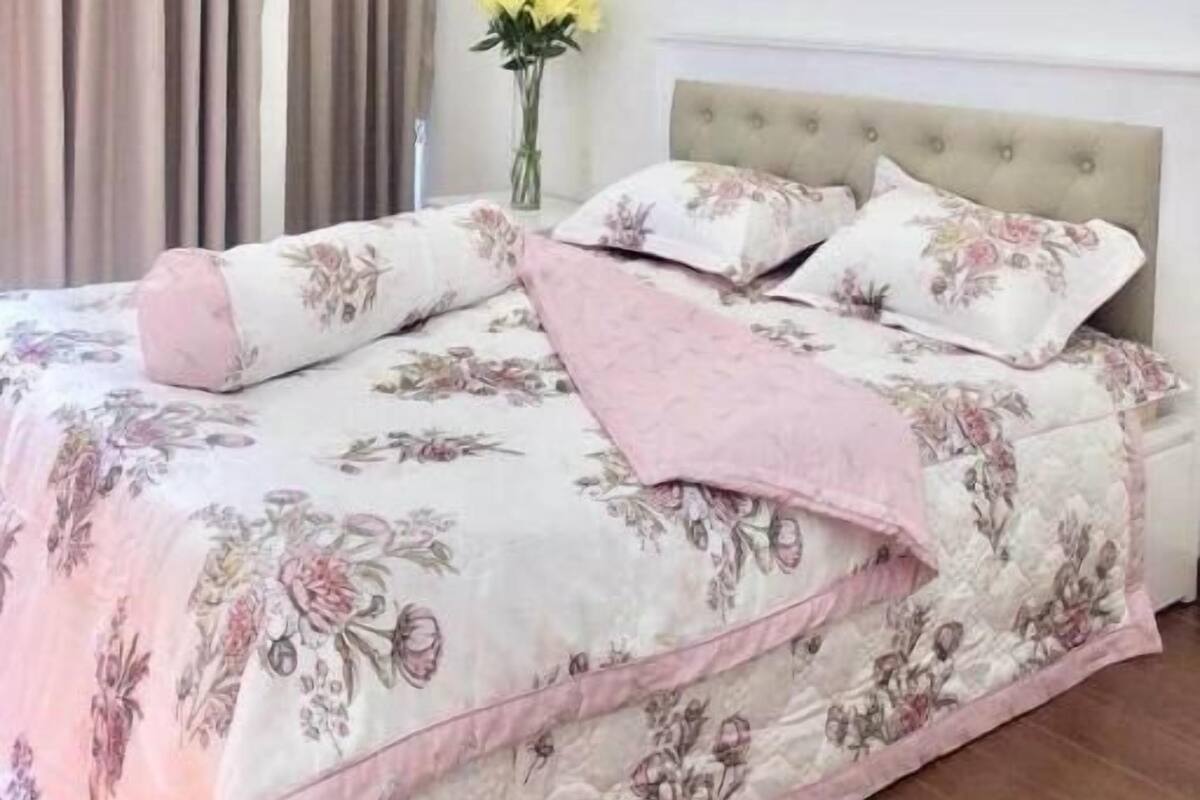 A bedroom with a bed, curtains, a vase with flowers, and a ceiling light.