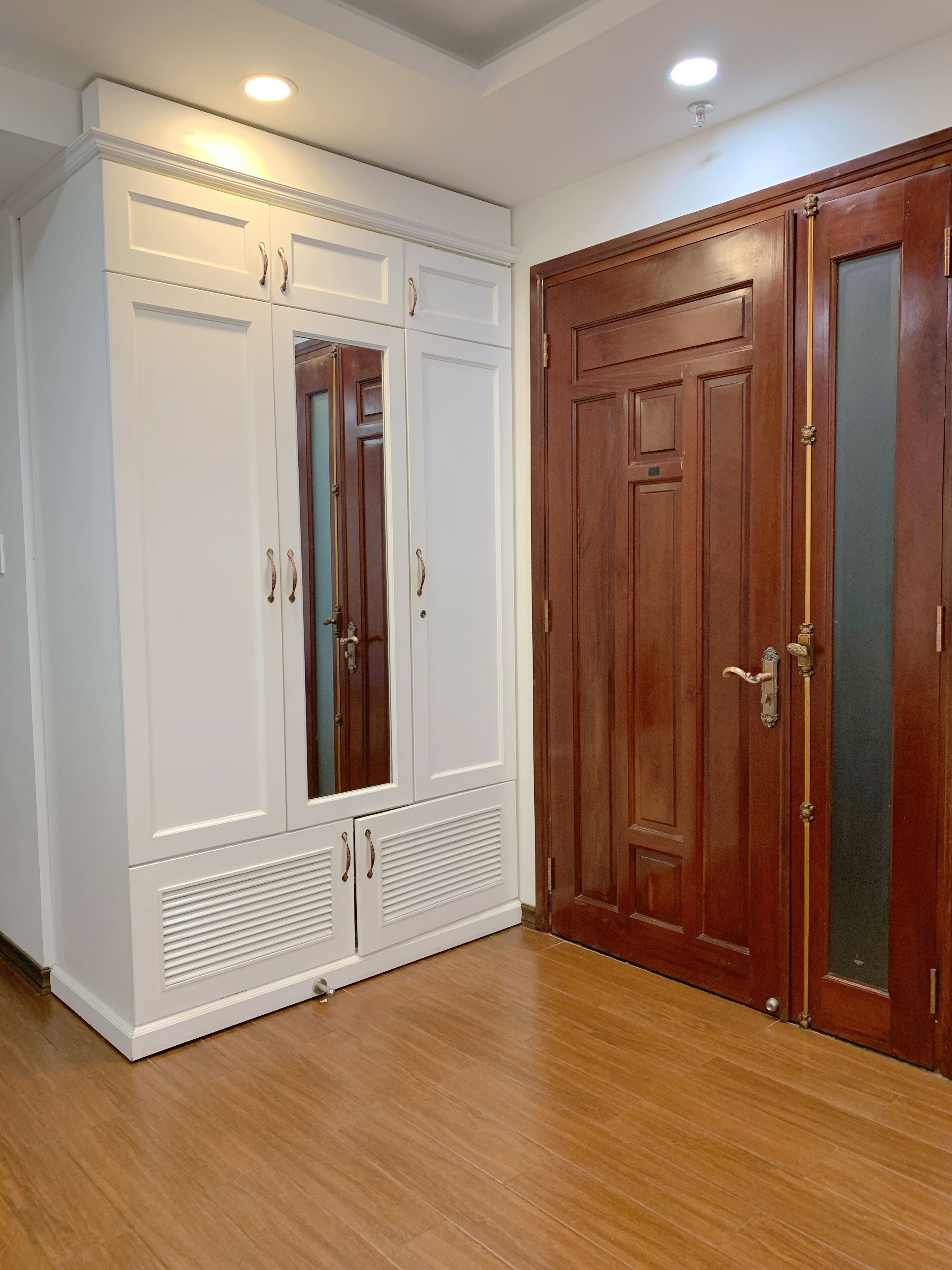 Quarto com um guarda-roupa grande e branco, uma porta de madeira e uma luminária no teto.