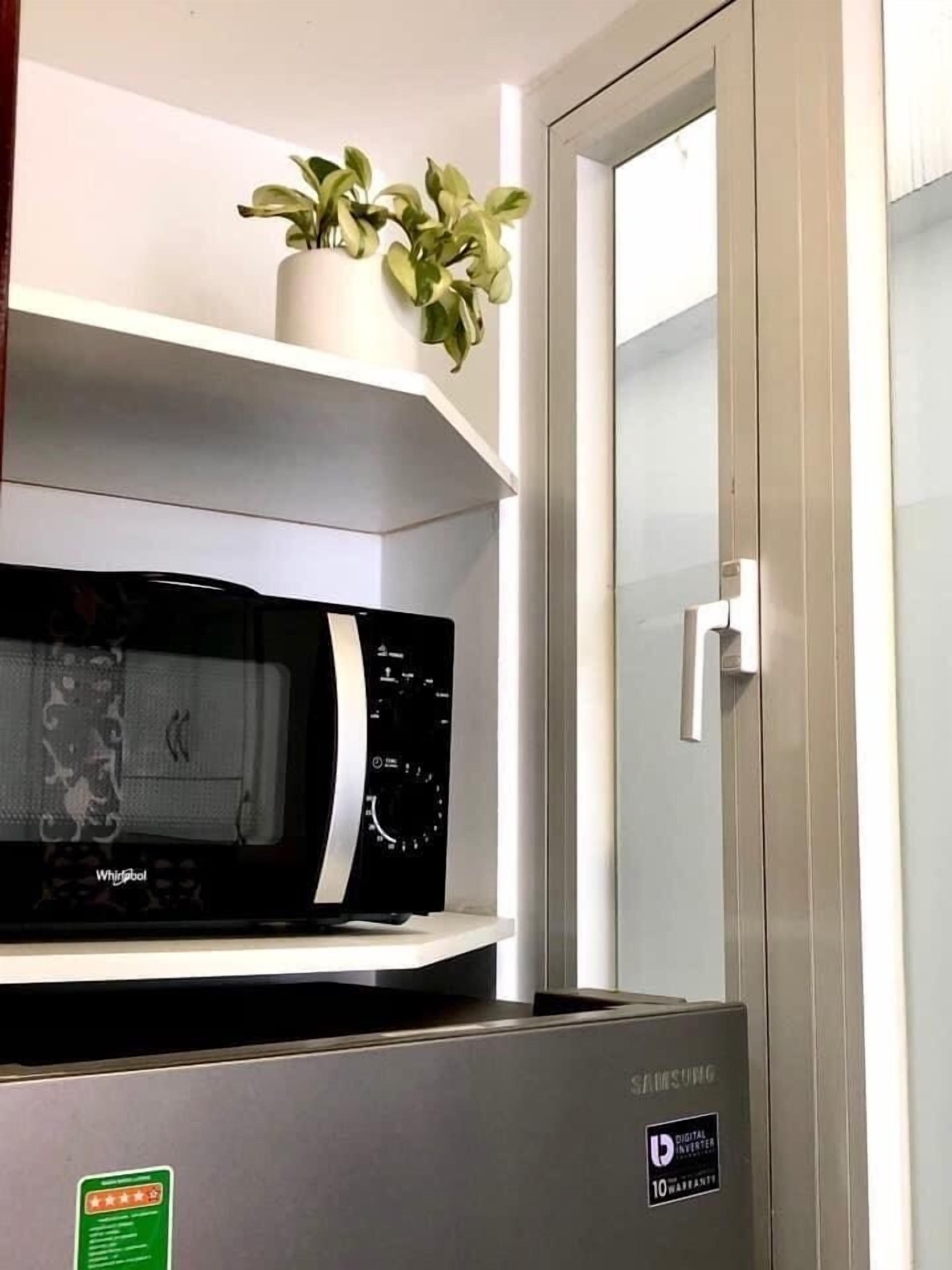 A kitchen with a microwave on a shelf, a Samsung refrigerator, and a potted plant on the wall.