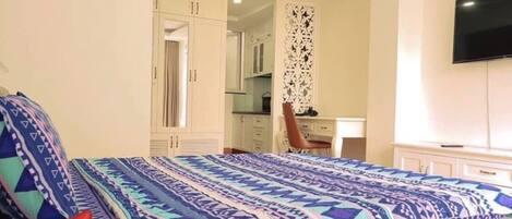 A bedroom with a patterned bedspread, a desk, and a television.