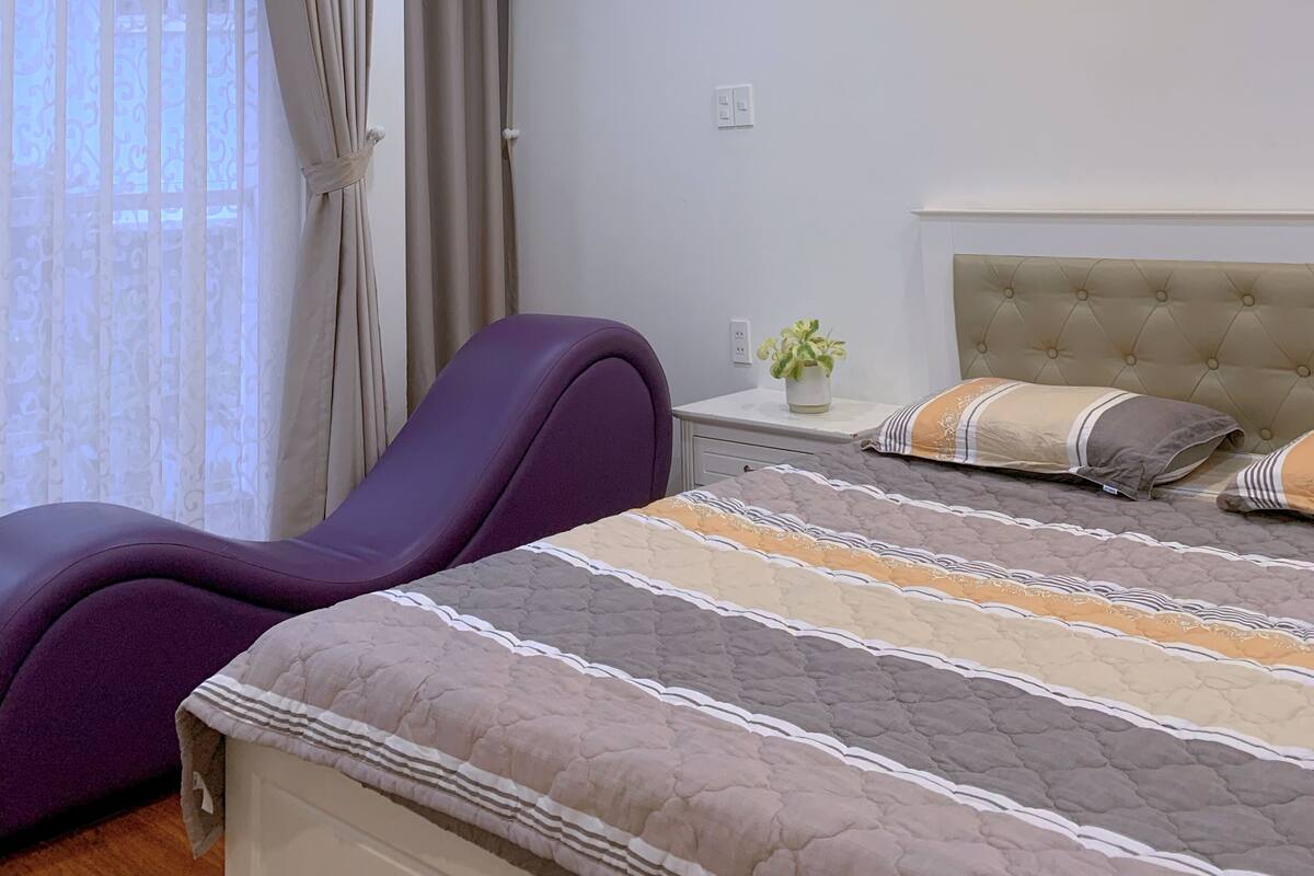 A modern bedroom with a bed, a chair, a bedside table with a plant, and a ceiling light.
