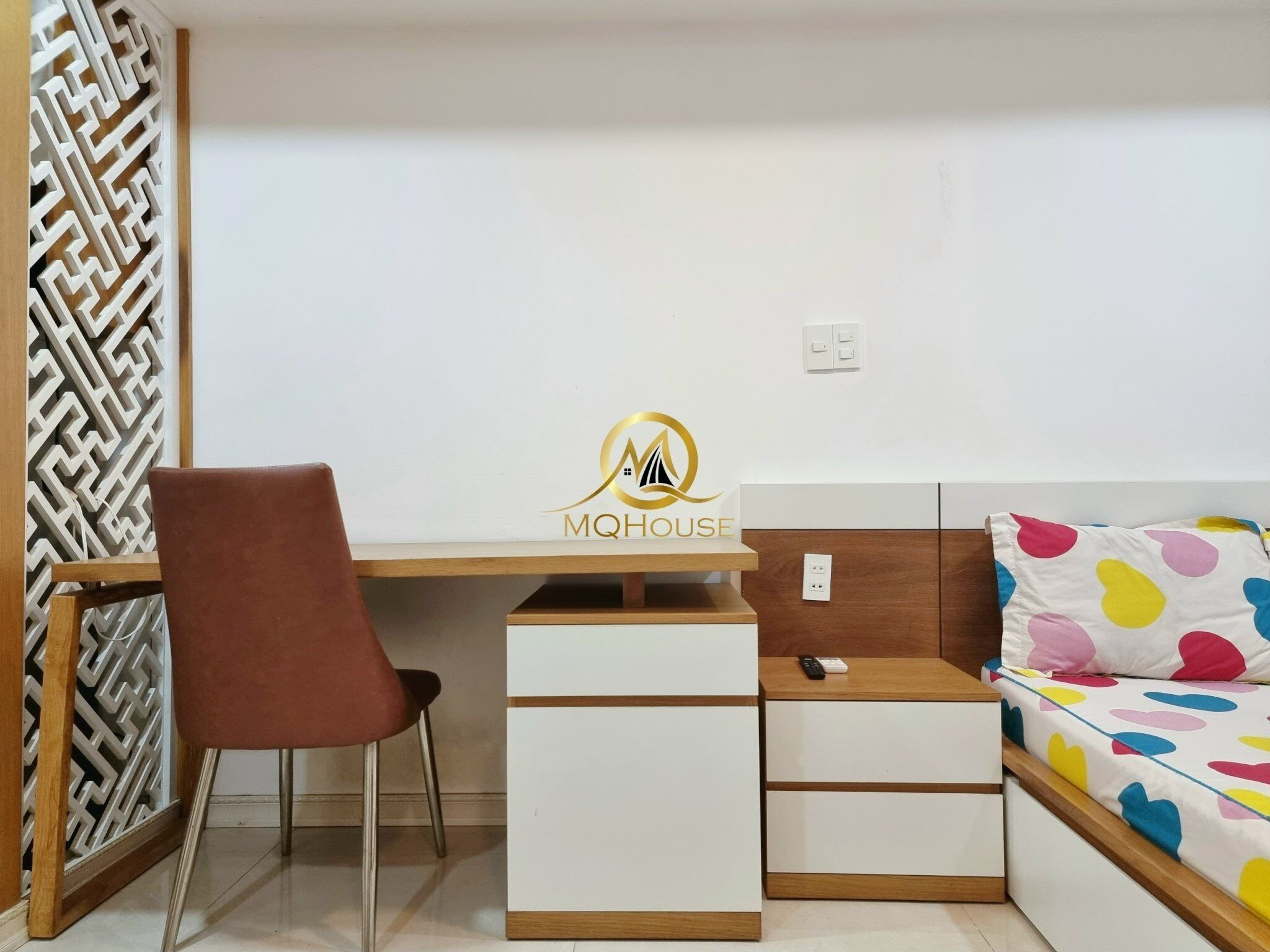 Une chambre avec un bureau, une chaise, un lit à motifs à pois colorés et un panneau décoratif mural.